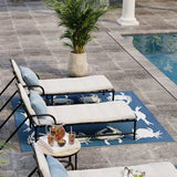 Outdoor lounge area with chairs, table, and plants by a pool.
