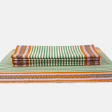 A rectangular placemat with a striped pattern in green and orange tones with four folded placemats on top of it.