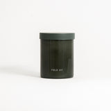 A green glass jar with a green lid labeled 'FIELD KIT' containing a home candle.