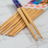 A close-up of several light brown bamboo chopsticks arranged on a white marble surface, with a blurred colorful package in the background.