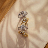 Four vintage-style rings with pearl accents on a beige fabric background