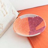 Woven bowl with orange and purple pattern on a white and orange surface