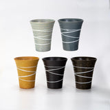 Five textured ceramic cups arranged in two rows on a white background. The top row features two gray cups, and the bottom row features one mustard yellow cup, one black cup, and one dark brown cup.