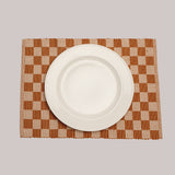 A woven placemat in a checker board pattern of orange and tan under a white porcelain plate.