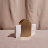 A gold-colored metal napkin holder with a white napkin placed in it, set against a neutral background.