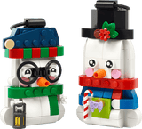Two LEGO-style snowman figures shown side by side on a plain white background. One snowman wears a blue hat with a red and green striped scarf, black glasses, and an orange carrot nose, holding a small lantern.