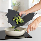 Person using a black bat-shaped cutting board to transfer broccoli into a pan on a stove.