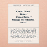 A rectangular nutrition facts label for a bar product, centered on a peach-pink textured background. The label reads 'INGREDIENTS + NUTRITION FACTS' and lists 'Cacao Beans', 'Dates', 'Cacao Butter', and 'Orange Essential Oil' as ingredients, with serving size 1/2 bar (30g) and nutrition details below.