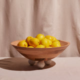 A large, round bowl made of wood with a smooth finish, filled with lemons and resting on three round feet.