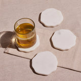 A set of four white marble coasters, each with a smooth surface and wavy edge, displayed against a neutral background.