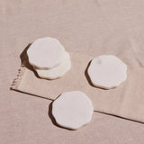 A set of four white marble coasters, each with a smooth surface and wavy edge, displayed against a neutral background.
