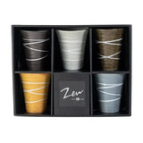 A set of five ceramic cups arranged in a black gift box, with the center compartment labeled 'Zen'. The cups come in five colors: black, light gray, dark brown, mustard yellow, and slate blue, each decorated with white wavy lines.