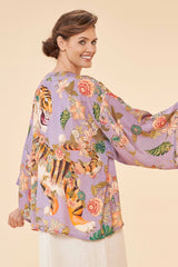 Woman wearing a colorful kimono-style garment with floral and tiger designs on a beige background