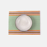 A rectangular placemat with a striped pattern in green and orange tones under a white ceramic plate.