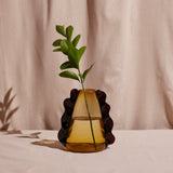 A conical amber glass vase with dark decorative elements placed against a pink textured background.