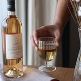 A hand holding a clear glass stemware cup with a striped pattern next to a bottle of wine.