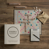 Scrabble game set on a wooden surface with tiles and score pad.