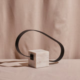 A modern loop table sculpture with a steel loop attached to a white marble base on a neutral background.