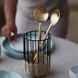 Two gold spoons in a metal and rattan utensil holder