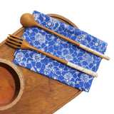 Wooden fork and spoon on a blue patterned napkin with a wooden bowl on a white background