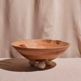 A large, round bowl made of wood with a smooth finish and resting on three round feet.