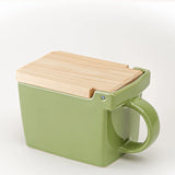 A square ceramic salt box in sage green with a hinged wooden lid, shown on a clean white background.