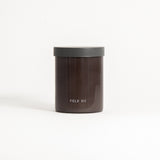 A brown glass jar with a black lid labeled 'FIELD KIT' containing a home candle.