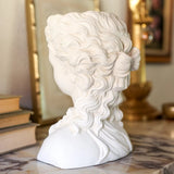 White marble bust of a classical figure on a marble surface with books and decorative items in the background.