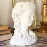 White classical bust sculpture on a marble surface with books and a mirror in the background.