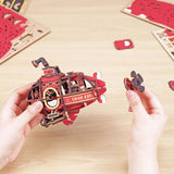 Red and gold 3D puzzle model of a submarine held by hands on a wooden surface.
