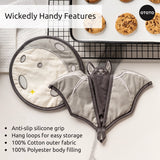 Bat-shaped oven mitt with anti-slip silicone grip and hanging loops, displayed with cookies on a cooling rack.