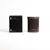 A brown glass jar with a black lid labeled 'FIELD KIT' containing a home candle.
