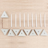 A set of white taper candles and wooden matches arranged on a light wood surface, with several small triangular white holders placed along the bottom.