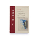 The book 'Furoshiki: And the Japanese Art of Gift Wrapping' by Tomoko Kanata, featuring a cream-colored cover with a vertical dark red spine and an illustration of a blue and white fabric gift wrap.