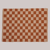 A woven placemat in a checker board pattern of orange and tan.