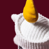 A close-up of a white ribbed plush toy or cushion with a bright yellow teardrop-shaped accent on top, set against a solid dark red background.