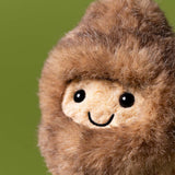 Close-up of a plush toy with a brown fuzzy exterior and beige face on a green background