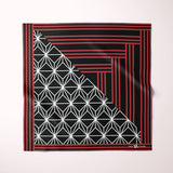 A square scarf with a geometric pattern, featuring a black background with red stripes, a red border, and a white geometric star-and-diamond motif in the lower-left quadrant, displayed flat against a light off-white background.