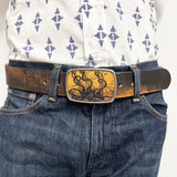 Person wearing a patterned shirt and blue jeans with a decorative belt buckle featuring an octopus attacking a ship