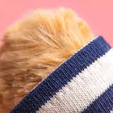 Close-up of a plush bear wearing a blue and white striped sweater against a pink background