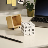 Cube with calendar text on a desk next to a laptop and pen