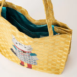A yellow woven tote bag with a textured circular pattern, featuring a white cat character wearing a red and blue kimono. The bag is shown open, revealing a teal satin lining, on a clean white background.