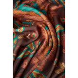 A close-up of draped fabric with an abstract painterly pattern in brown, orange, teal, and beige tones.
