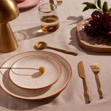 Two white stacked stoneware plates with a brass wavy handled knife, fork, and spoon.