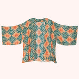 A 3/4 sleeve kimono-style jacket with a vibrant teal and orange geometric pattern, displayed flat against a pale pink background.