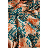 A close-up of draped fabric with a repeating ornamental floral pattern in teal, orange, and cream.