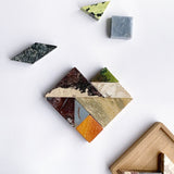 A colorful gemstone tangram puzzle with seven pieces, some in shades of red, orange, yellow, green, blue, and gray, displayed on a wooden board.