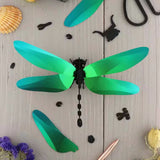 Green and black paper dragonfly-shaped decoration on a wooden surface with small objects.