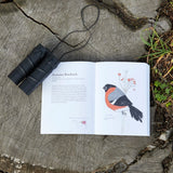 Open book with bird illustration on a wooden surface next to binoculars