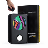 A black Klydo Clock with a colorful abstract face is shown in front of its black retail box. A hand is holding the small black remote above the clock.